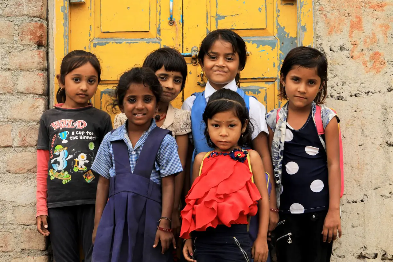 A group of children standing and smiling in front of a bright yellow door