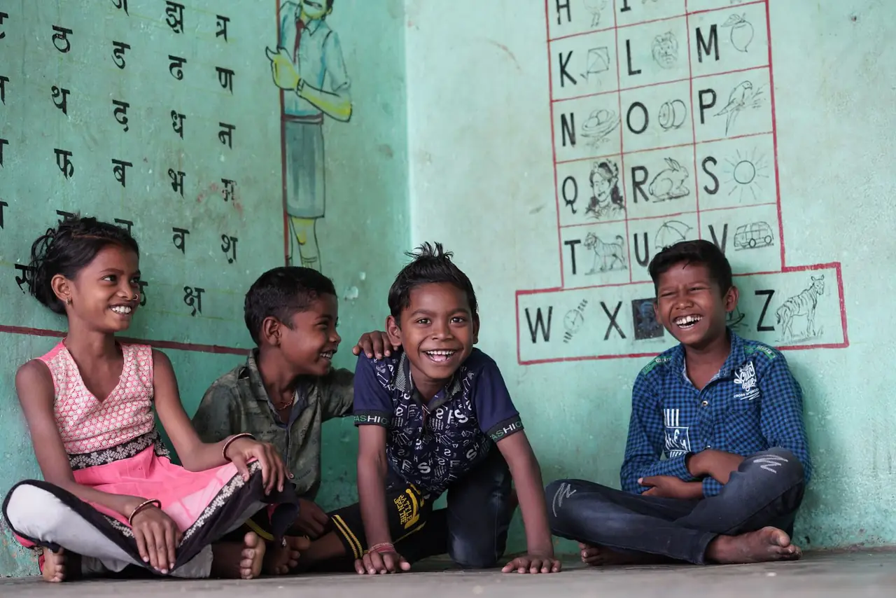 Four children sitting against a green wall, laughing together